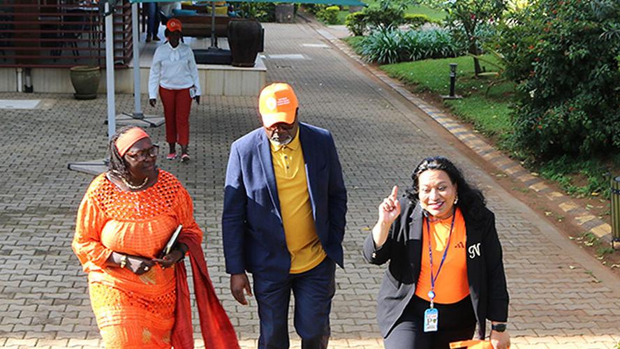 A man and two women walking down a path. All three are wearing orange coloured clothing.