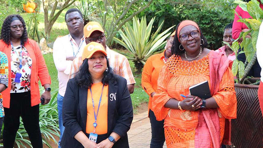 A group of people standing together and smiling watching what is happening on a stage which is not pictured.