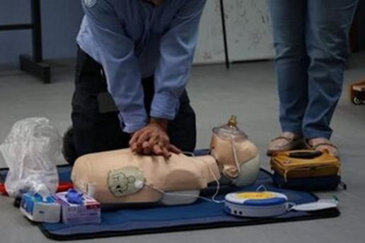 A person applying CPR to the CPR doll on the floor while a person looks on