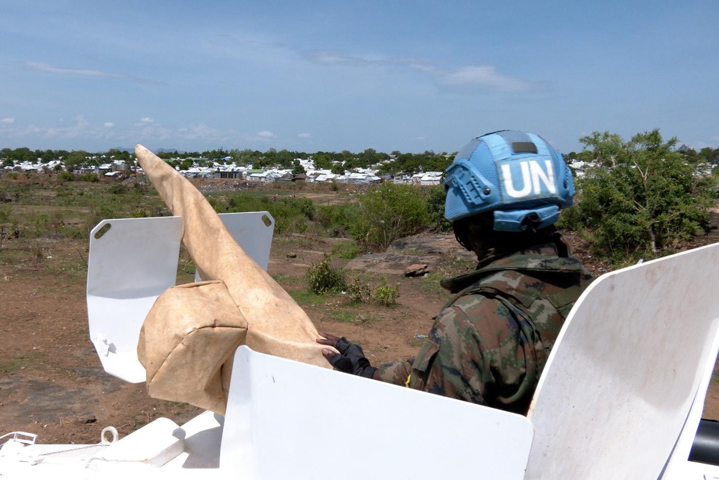 Rwandan peacekeepers patrol around camps for displaced communities to strengthen security as political tensions rise and clashes continue between armed forces in pockets of the country. A peacekeeper peering out of the top of a tank across a grassy field. The peacekeeper is facing away from the camera.